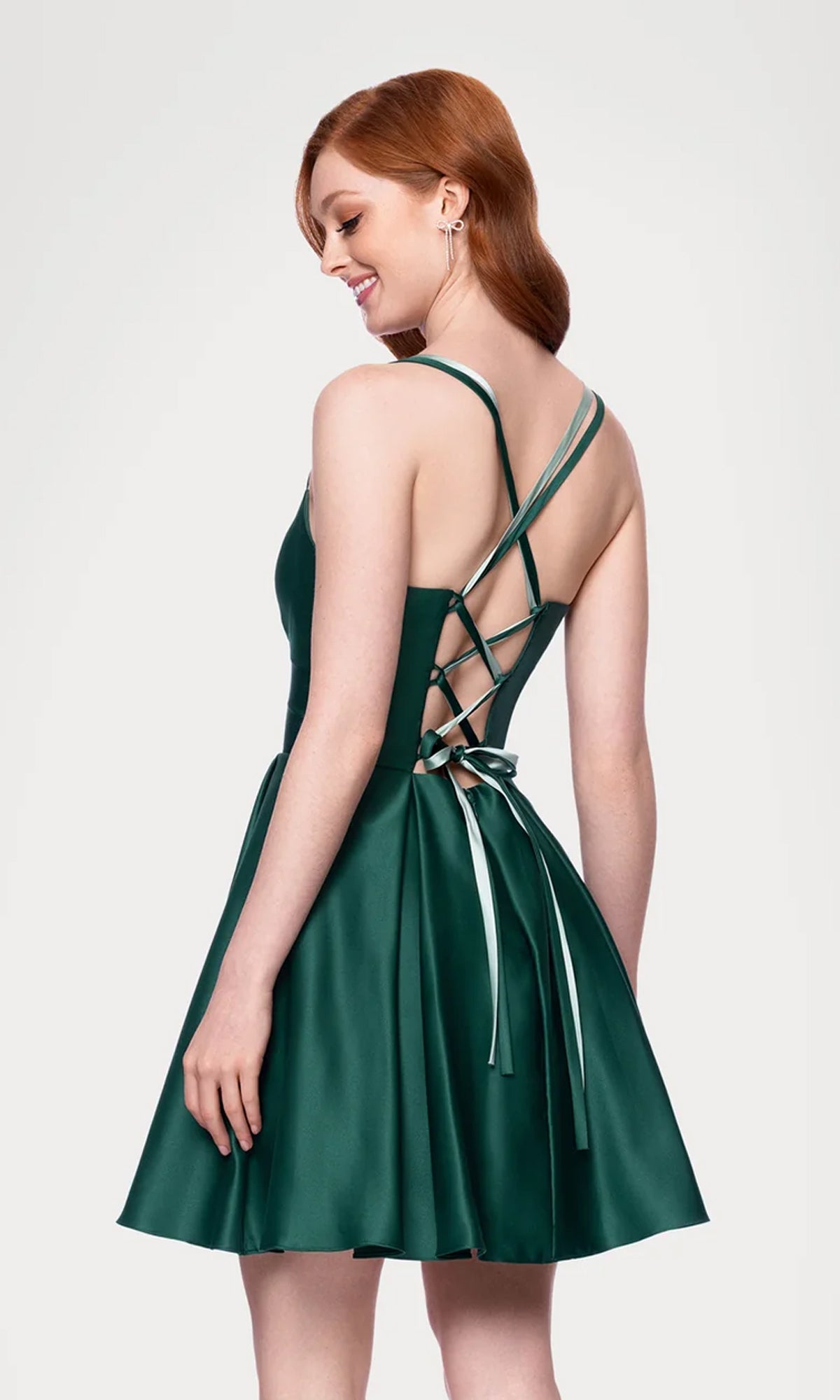 Woman wearing the Hunter Green Mini Hoco Dress (Blondie Nites 4927BN) with an A-line silhouette, lace-up crisscross back straps, and ribbon tie, standing and smiling against a plain background.
